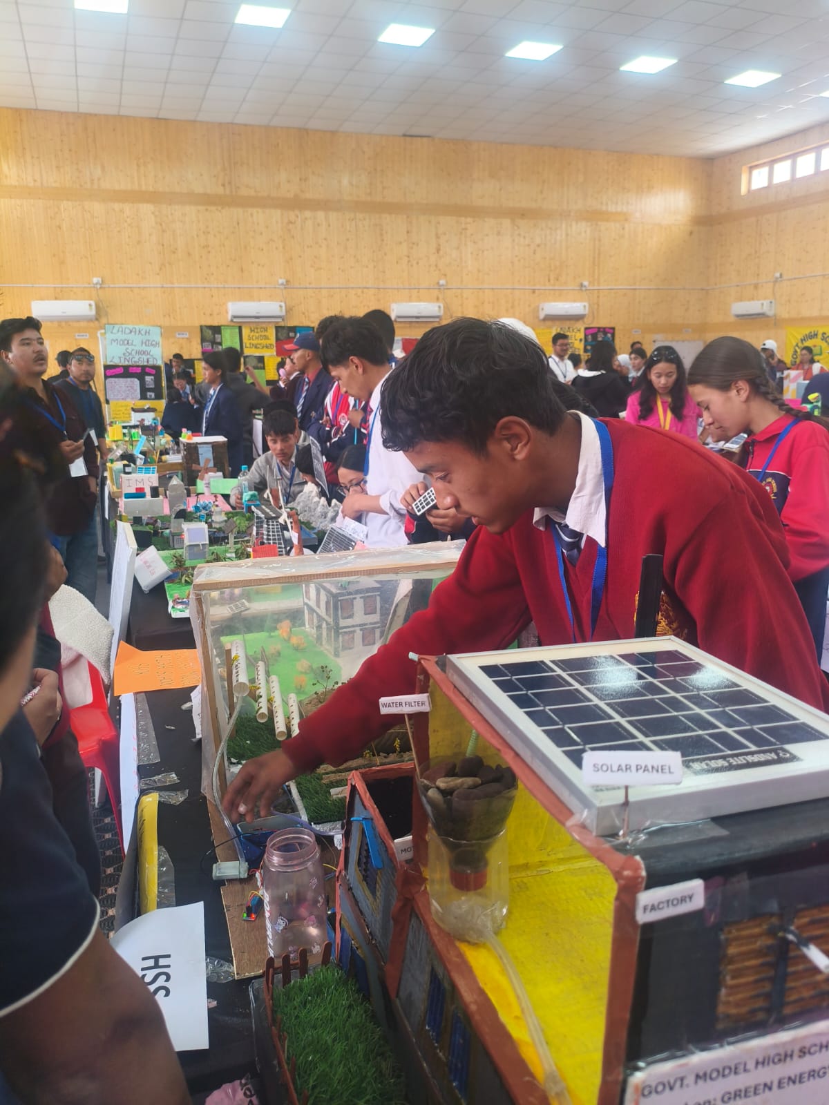 Working Model — Solar Powered Water Filter Student in red uniform demonstrating a solar-powered water filter working model at a science exhibition